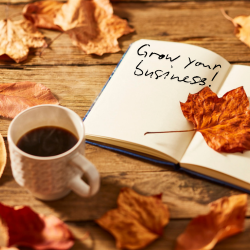 Open notebook reading 'Grow your business!' beside a coffee cup and autumn leaves, symbolising business growth during the autumn season