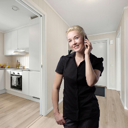 Woman making a phone call in a home hallway, with an adjoining kitchen visible.
